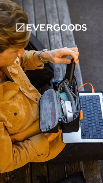 A top-down 9:16 view showing a person using a tech organizer pouch to manage cords and power banks while sitting in a public space.