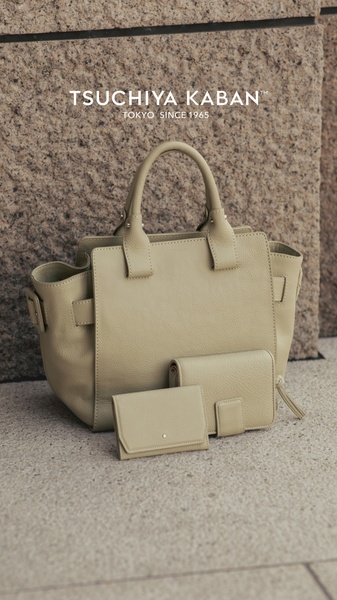 A high-end lifestyle shot of a leather handbag and matching wallets placed on stone, emphasizing a neutral color palette and clean design.