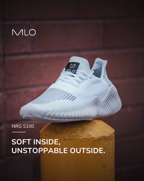 A high-contrast 4:5 social media creative featuring a single white sneaker balanced on a yellow bollard against a dark brick backdrop.
