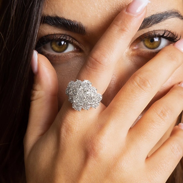 A luxury engagement ring is presented in a close-up lifestyle shot with the model's hand partially covering her face to create intrigue.