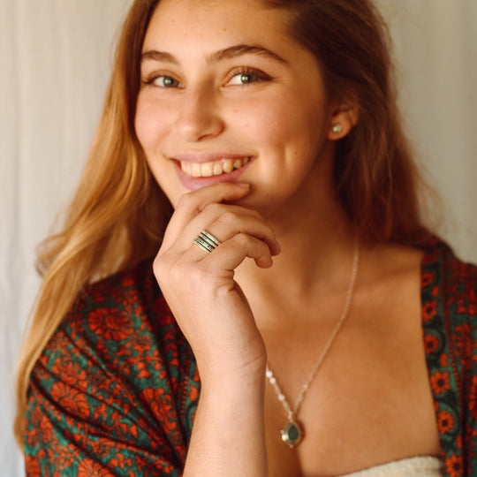A close-up portrait of a woman wearing silver stacking rings, focusing on natural beauty and jewelry placement.