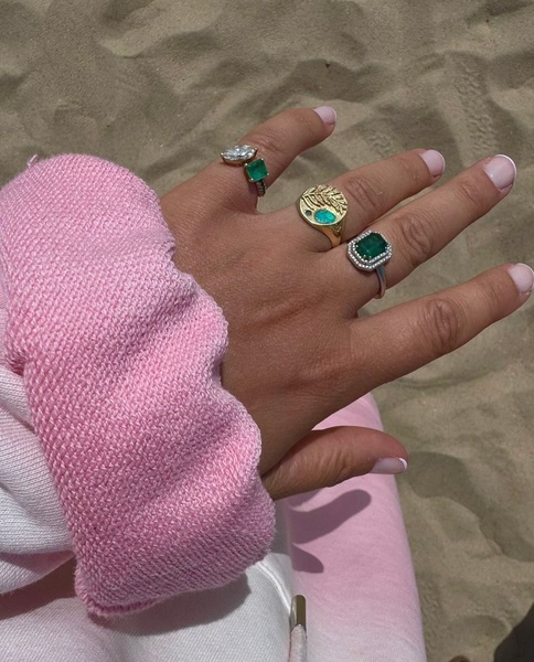 A close-up, high-angle shot showing a hand wearing multiple gemstone rings against a sandy beach background.