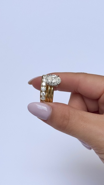 A close-up, high-detail shot of an engagement ring held between fingers, emphasizing the setting and diamond clarity against a clean, neutral background.
