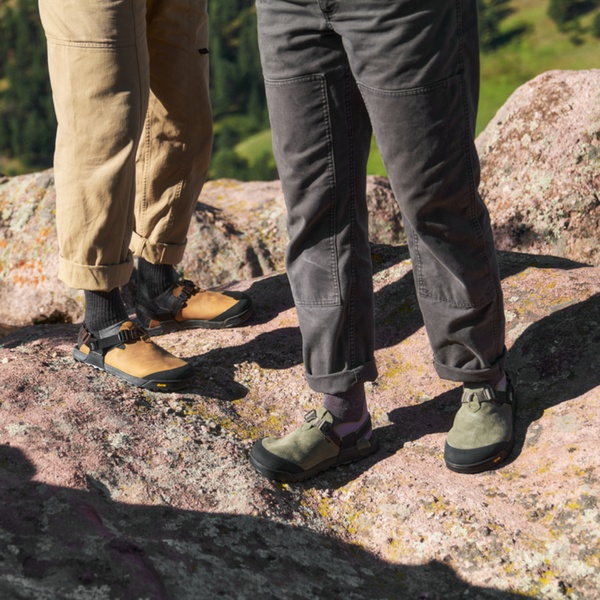 A close-up shot focusing on two individuals wearing rugged hiking sandals while standing on a rocky mountain terrain.
