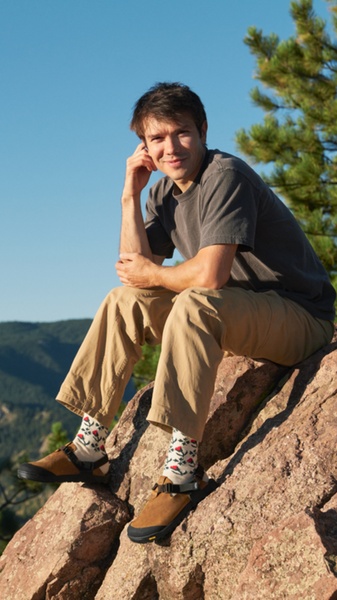 This ad features a model wearing patterned socks and outdoor clogs while sitting on a rock in a natural, sunlit setting.