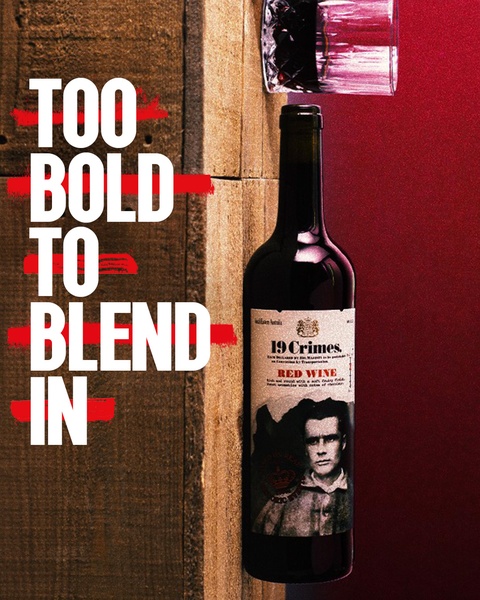 A high-contrast advertisement for red wine featuring a vertical, text-heavy hook placed alongside a bottle and a glass on a wooden surface.