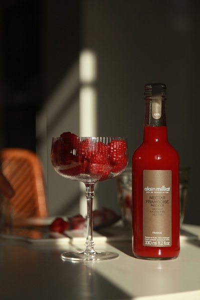 A close-up studio shot of a glass of raspberry nectar next to a bottle, emphasizing premium textures and natural light.