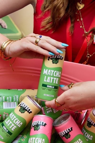 A close-up, high-engagement lifestyle shot featuring hands holding a matcha latte can surrounded by multiple product cans in a bright, casual setting.