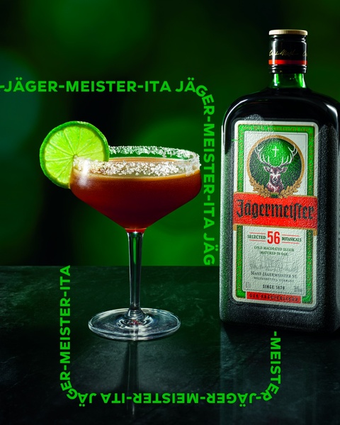 A high-quality product shot featuring a cocktail with a lime garnish next to a bottle of Jagermeister, emphasizing brand identity through text placement.