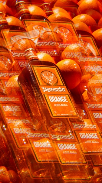 A high-impact product photography shot featuring a bottle of orange liqueur surrounded by fresh oranges, using a deep orange and amber color palette.