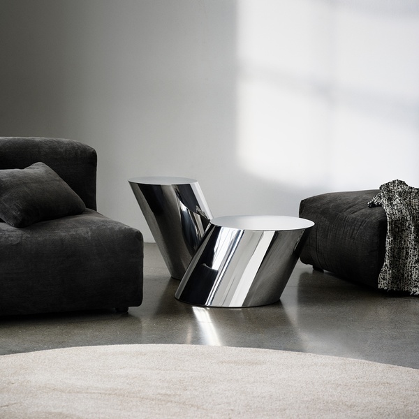 A high-end, studio-lit photograph featuring two metallic chrome side tables in a modern, moody interior setting.