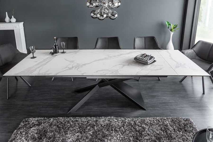 An elegant wide-angle shot of a marble-top extendable dining table with dark velvet chairs, set against a dark grey architectural background.