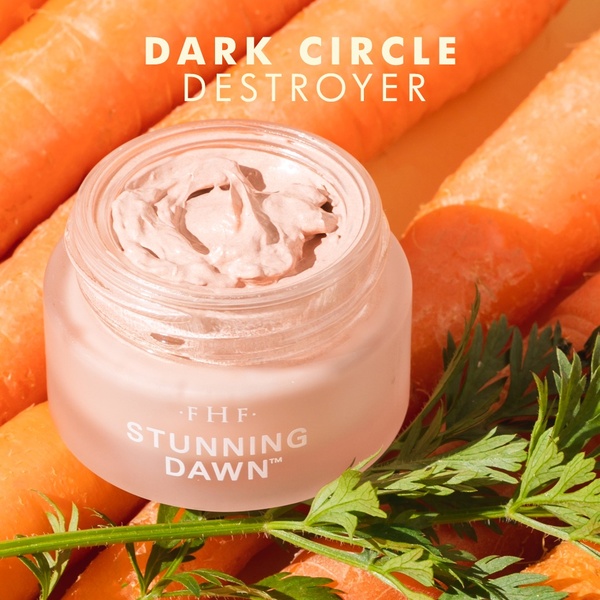 A close-up, top-down shot of an eye cream jar nestled in a pile of fresh, vibrant orange carrots to imply natural effectiveness.