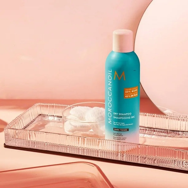 A clean, studio-lit photograph of a Dry Shampoo bottle placed on a glass tray against a soft pink background.