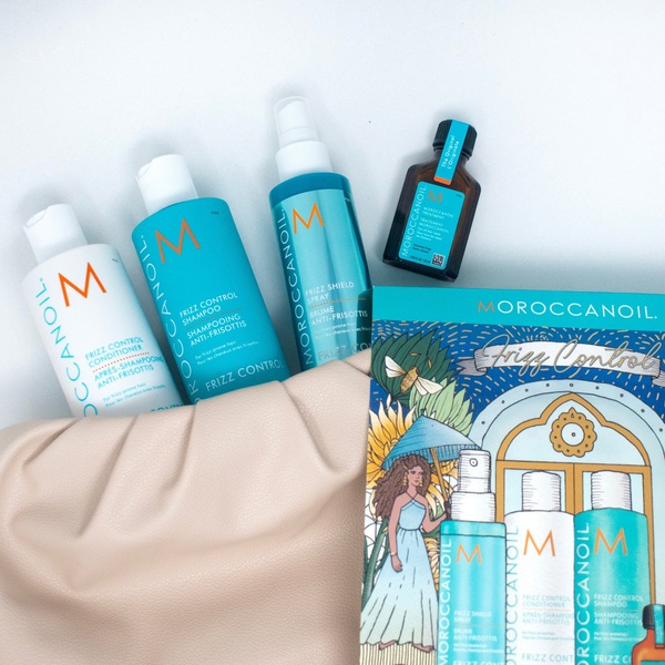 A high-end, top-down flat lay featuring the Moroccanoil Frizz Control hair care collection displayed alongside a neutral-toned bag.