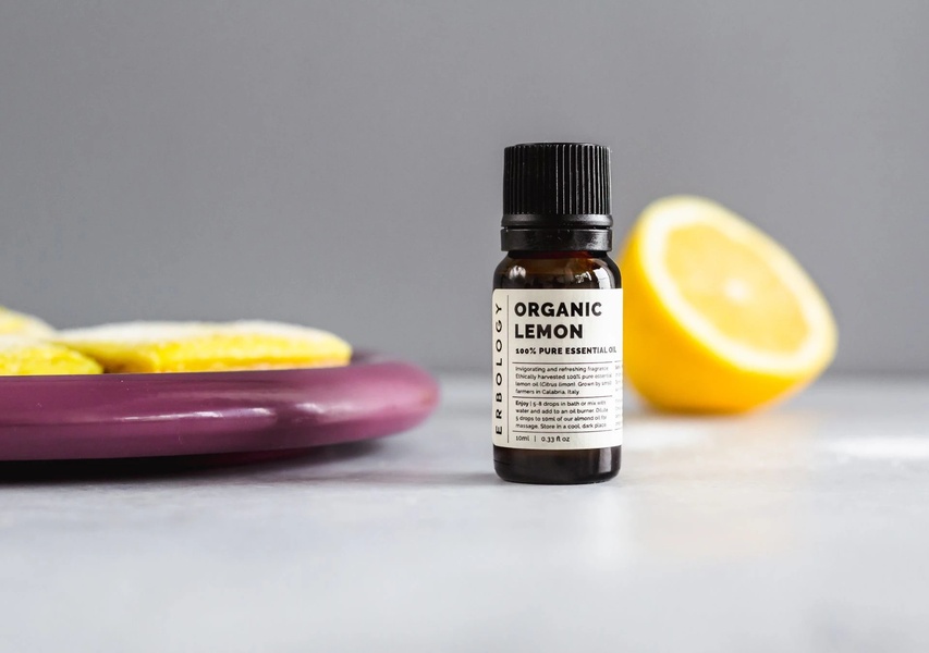 A high-clarity, minimalist studio shot of an essential oil bottle placed next to a fresh lemon slice and a dark plate.