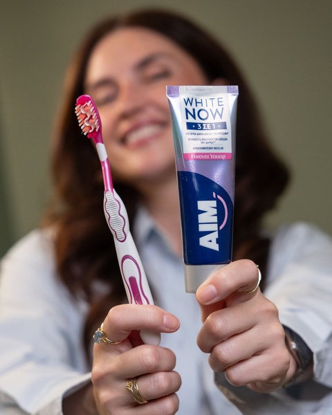 A close-up shot featuring a person holding a toothpaste tube and toothbrush, showcasing the product clearly as the central hero.
