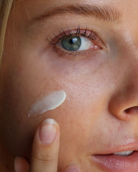 A close-up shot capturing a finger applying a smooth, white face cream onto a person's cheek to highlight texture and product application.