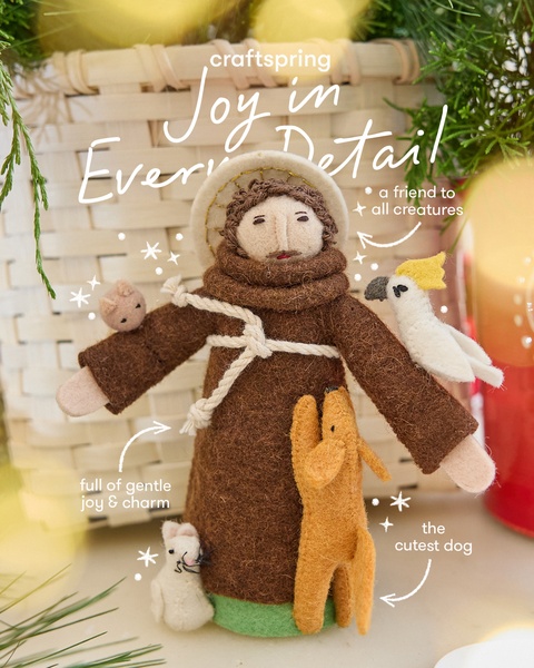 A close-up, high-quality photograph of a handcrafted felt figurine of a saint accompanied by several small animal felt friends, staged against a warm, rustic backdrop.