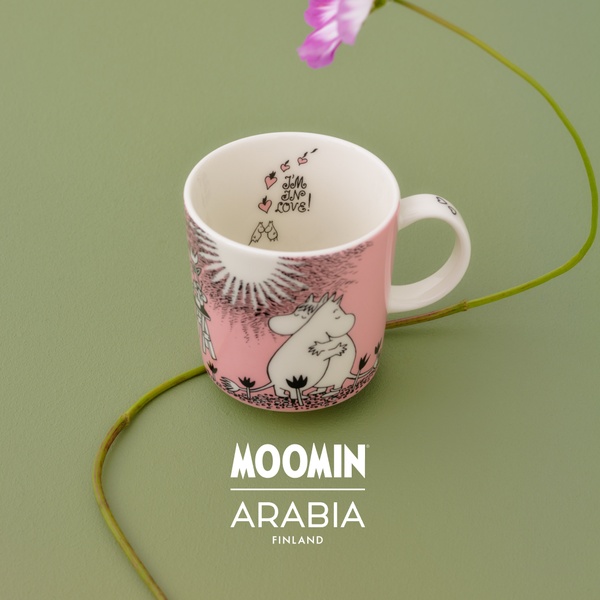 A clean, minimalist product hero shot of a Moomin character mug placed on a solid green background with a single flower stem.