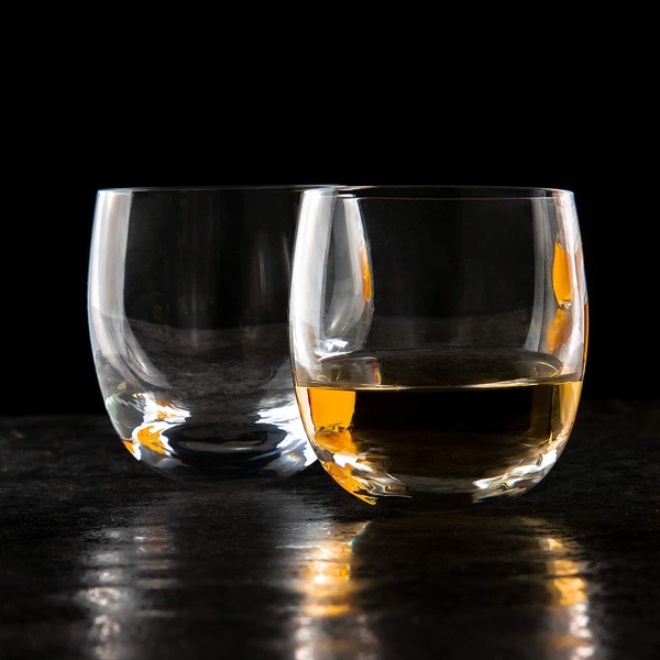A high-contrast, professional product photograph of a clear whiskey glass, one filled with amber liquid, set against a dark background.