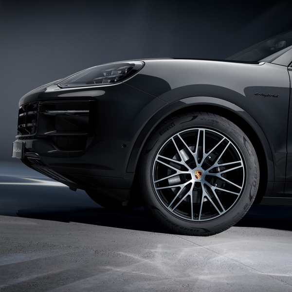 A high-contrast, dramatic studio shot focusing on the front wheel and headlight assembly of a luxury e-hybrid SUV.