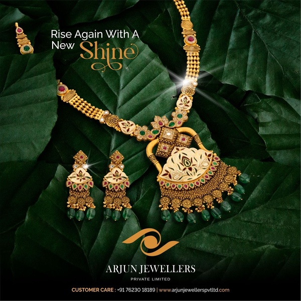A high-end jewelry set featuring a gold necklace and earrings laid out against deep green organic foliage.