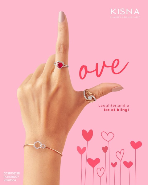 A close-up photograph of a hand positioned in an 'L' shape to mimic the word 'love', adorned with a ruby heart ring, gold ring, and hexagonal bracelet.