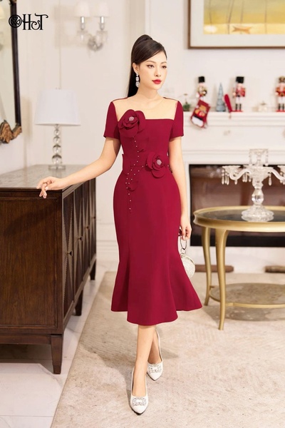 A high-quality, full-body portrait featuring a model in a deep burgundy evening dress, set in a refined, warm-toned interior.
