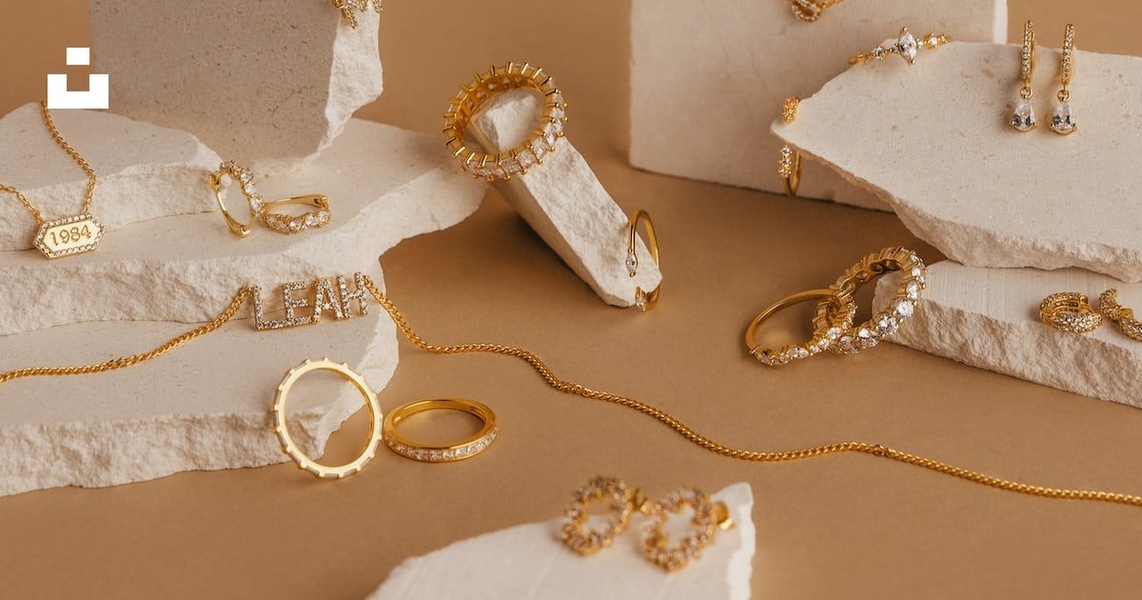 A high-quality studio shot of gold jewelry including rings, necklaces, and earrings arranged on textured stone blocks for a premium feel.
