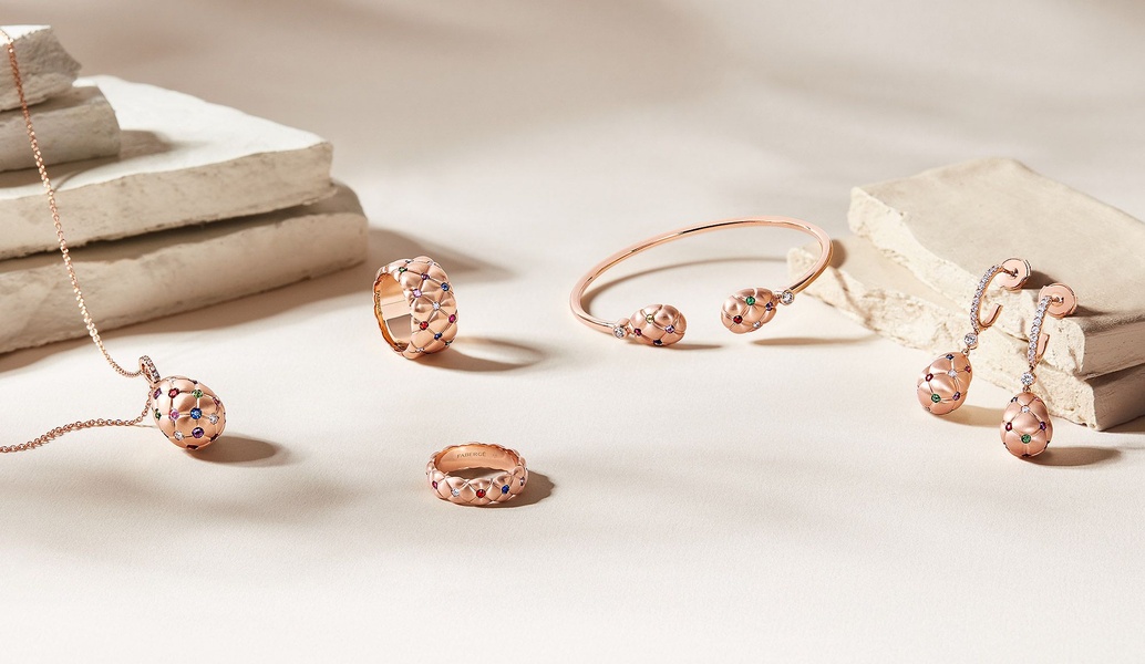A refined product hero shot featuring a gold jewelry set with colorful gemstone accents arranged on textured stone surfaces in soft lighting.