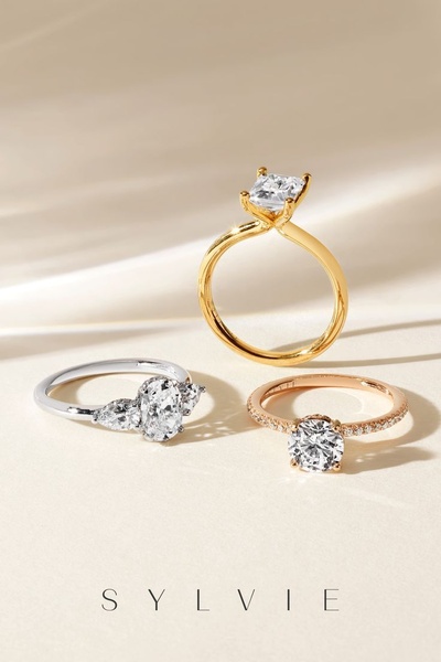 A high-end visual featuring three distinct diamond ring styles arranged on a clean, neutral-toned fabric background to emphasize product design.