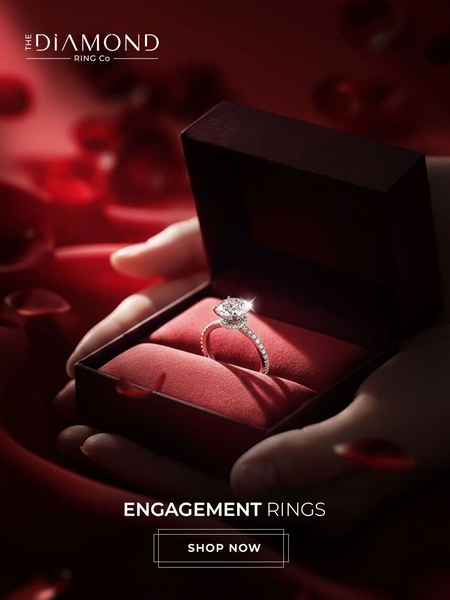 This creative features an engagement ring placed inside an open box, held by hands and surrounded by soft red petals to evoke emotion and luxury.