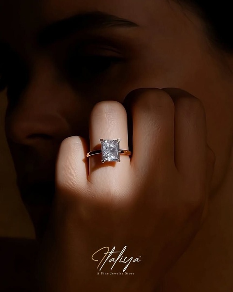 A high-end, close-up photograph of an engagement ring on a person's hand, utilizing dramatic spotlighting to emphasize the diamond's brilliance.