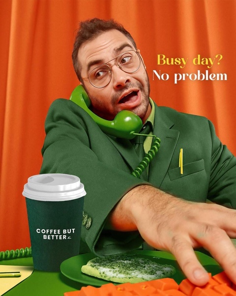 A man in a green suit handles a busy office phone while a cup of coffee and a green cookie sit on his desk, promoting a better coffee experience.