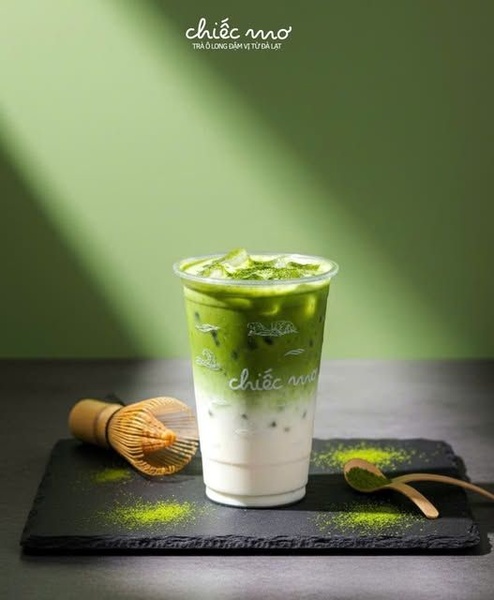 A high-contrast, minimalist shot of a fresh matcha latte on a slate tray, featuring traditional tea preparation tools for an authentic aesthetic.