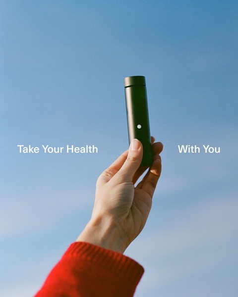 A hand holds a sleek green portable wellness bottle against a clear blue sky, emphasizing simplicity and a healthy on-the-go lifestyle.