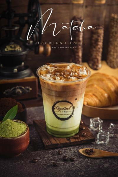 A high-quality studio shot of a layered Matcha Espresso Latte on a wooden coaster with coffee beans and a croissant in the background.