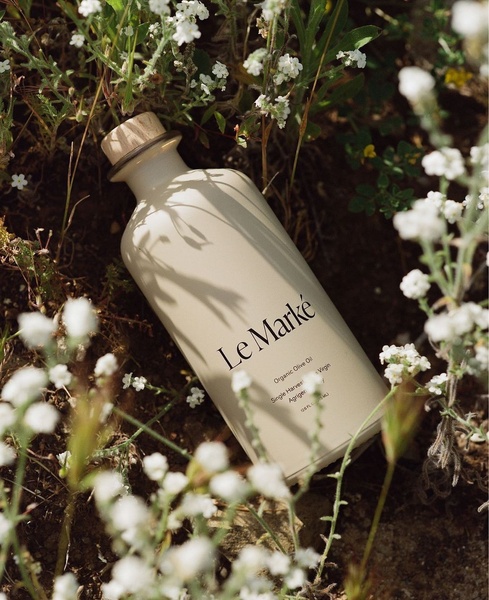 A high-end, top-down shot of a branded olive oil bottle resting in a field of small white flowers, emphasizing purity and natural sourcing.