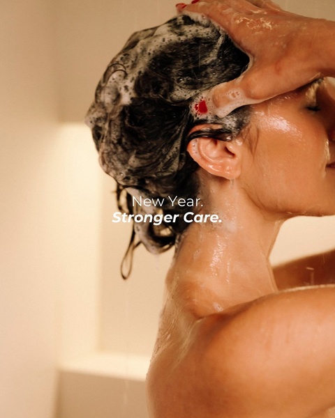 A close-up, high-sensory lifestyle shot of a person using shampoo in a warm, inviting bathroom setting.