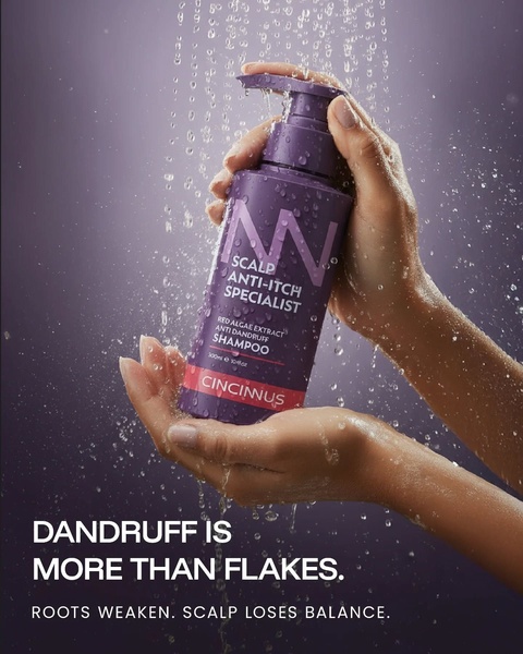 A high-contrast, atmospheric image of a hand holding a purple shampoo bottle under a stream of water, focusing on root health and scalp balance.