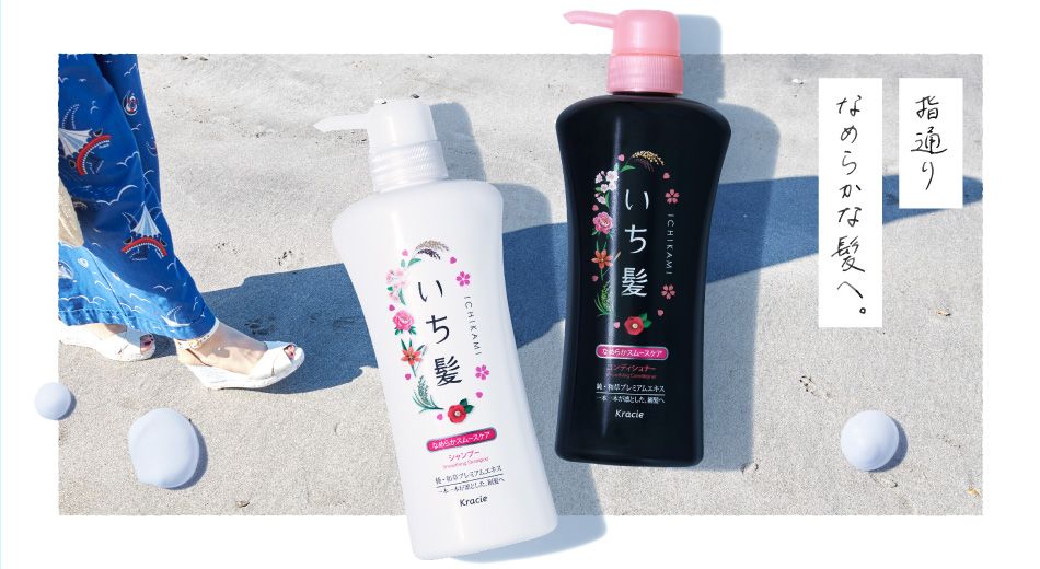 A high-key, minimalist product hero shot featuring shampoo and conditioner bottles on a sandy beach.