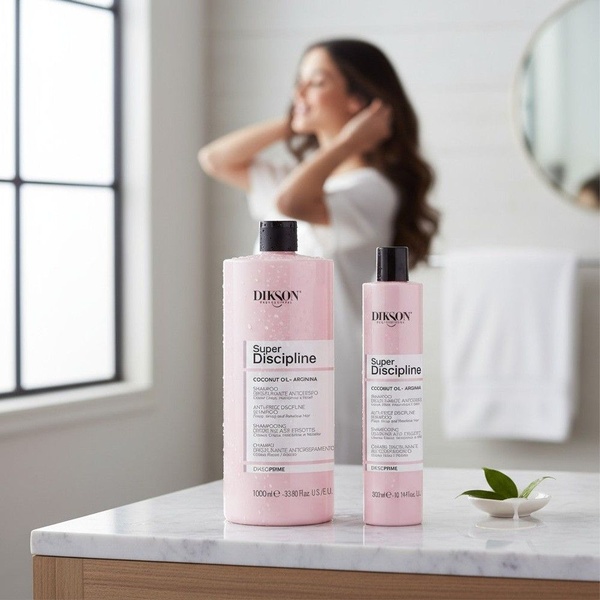 A high-quality, bright, and airy product hero shot featuring hair care bottles on a marble surface with a blurred model in the background.