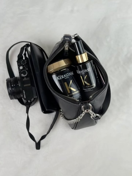 A high-end, top-down shot of a hair care serum and treatment jar inside a designer handbag, paired with a camera for a premium aesthetic.
