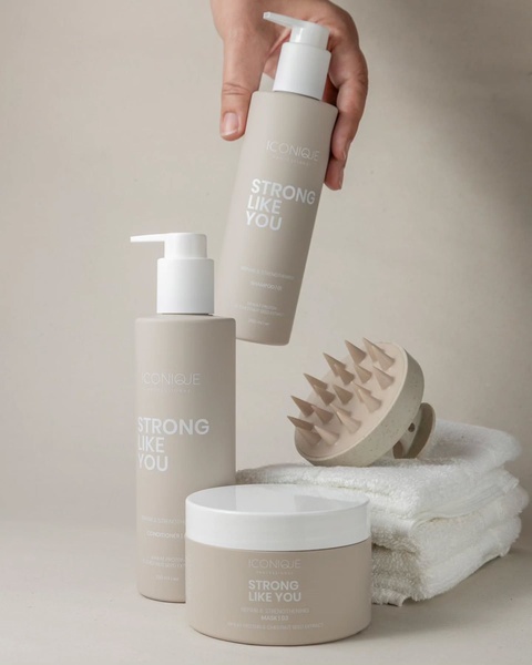 A clean, studio-lit composition featuring three hair care product bottles and a scalp massager against a neutral background, held by a model.