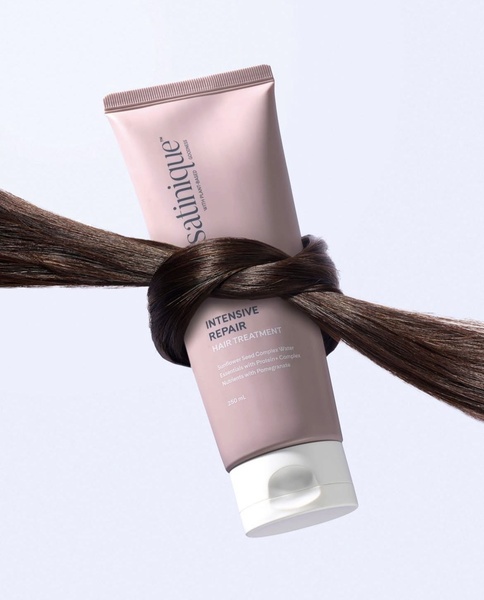 A high-end studio shot featuring a hair treatment tube wrapped in a literal knot of brown hair, emphasizing product benefits through a clean, metaphorical visual.