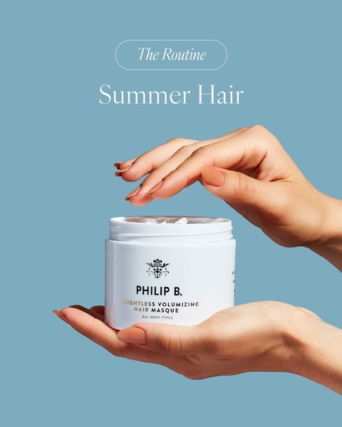A clean, high-contrast studio shot of hands holding a branded hair masque jar against a solid blue background.