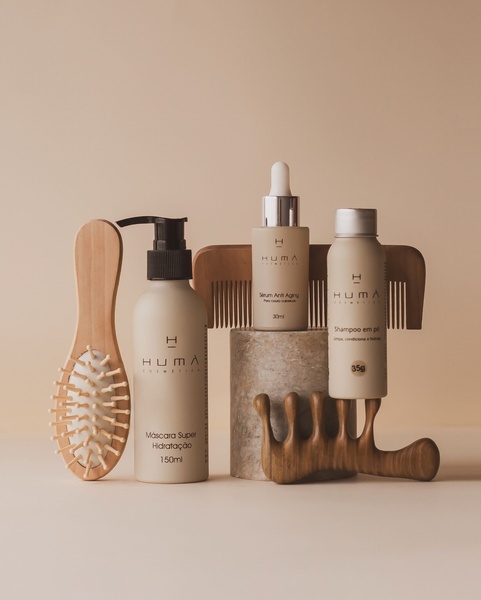 A clean, minimalist product hero shot featuring a hair care set arranged on a stone pedestal with wooden styling tools.