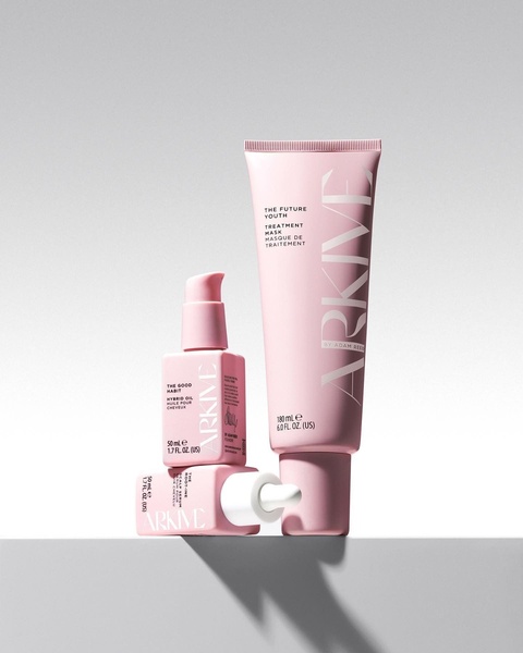 A high-end studio shot featuring three hair treatment products arranged in a clean, balanced composition against a soft grey background.