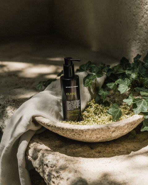 A high-end product shot of Botanical Shampoo placed in a stone bowl with organic herbs, emphasizing purity and natural sourcing.